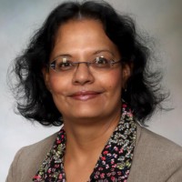 Portrait of a researcher with glasses and curly hair, wearing a floral blouse and blazer.