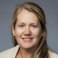 Portrait of a researcher smiling, wearing a white jacket against a gray background.