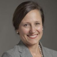 Portrait of a smiling woman in a gray blazer with pearls.