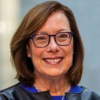 Portrait of a smiling woman with glasses and shoulder-length brown hair, likely from a cancer research organization.