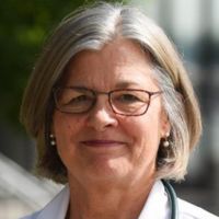 Portrait of a woman with gray hair and glasses, likely a healthcare professional.
