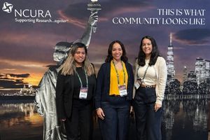 Three women posing in front of a backdrop featuring the Statue of Liberty and skyline, representing the Alliance for Clinical Trials in Oncology.