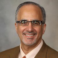 Portrait of a smiling male researcher wearing glasses and a tan jacket.