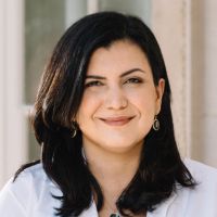 Portrait of a woman with dark hair smiling, likely a researcher in a clinical setting.